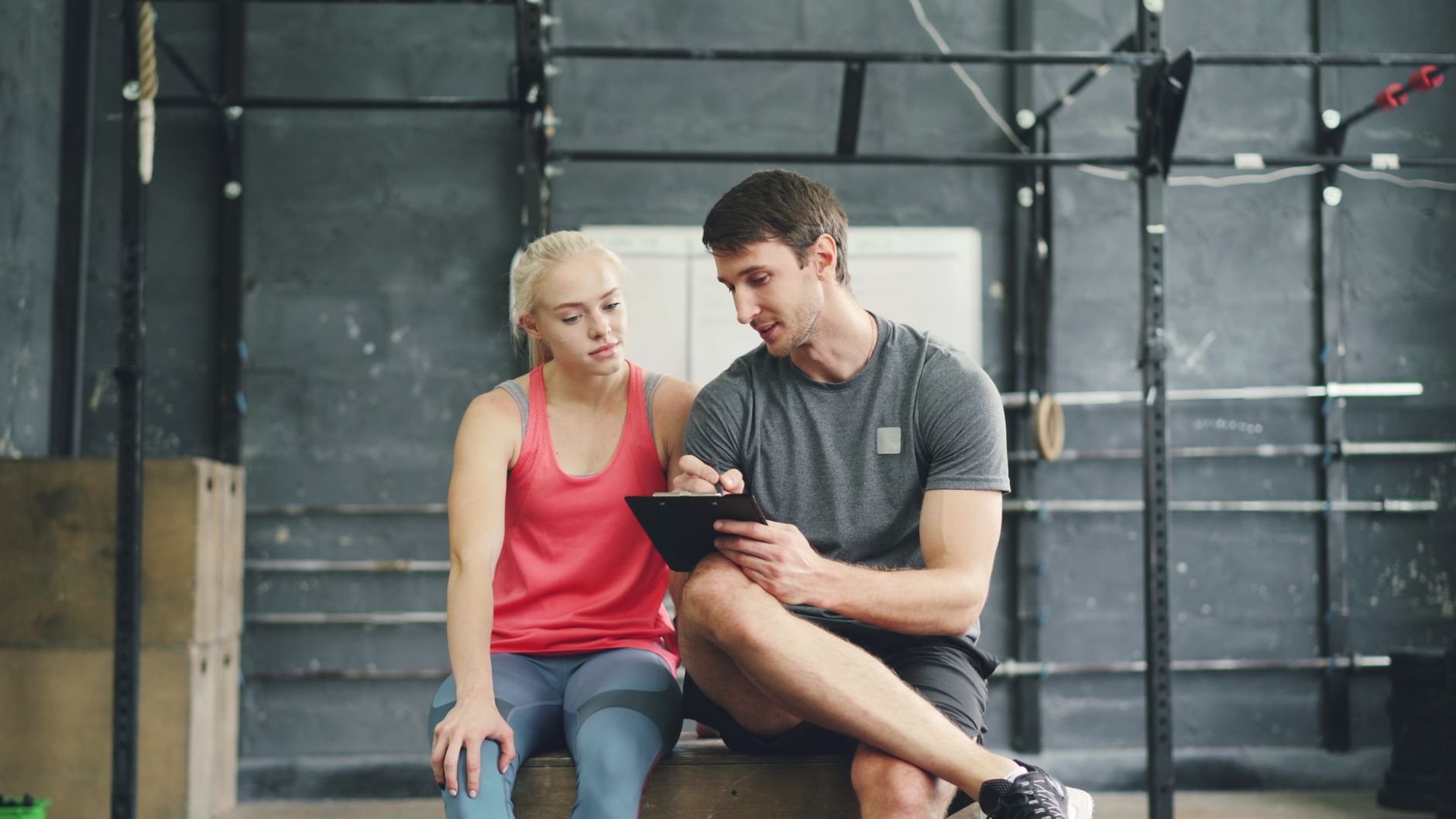 Personal trainer with client reviewing workout plan in gym setting.